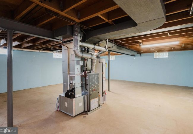 Basement utility area with a furnace and large metal ducts, exposed ceiling beams, and blue walls.