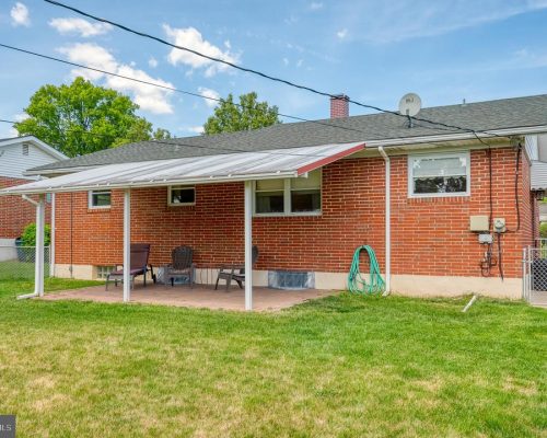 Backyard view of a red brick house with a covered patio and outdoor seating on a brick slab