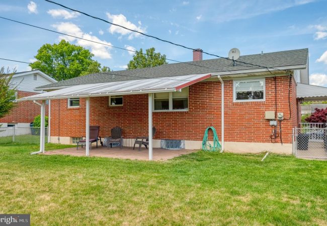 Backyard view of a red brick house with a covered patio and outdoor seating on a brick slab