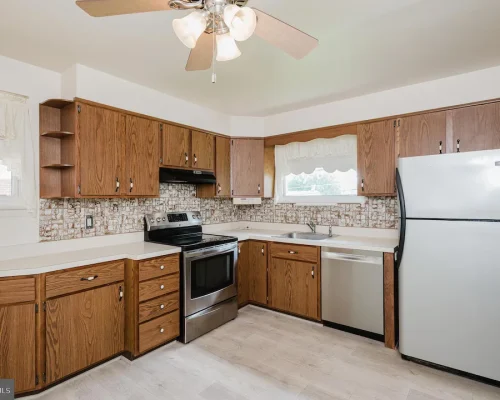 U-shaped kitchen with oak cabinetry, white countertops, stainless steel range and dishwasher, and a large fridge against the right wall.