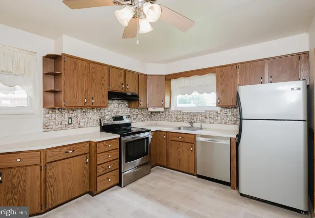 U-shaped kitchen with oak cabinetry, white countertops, stainless steel range and dishwasher, and a large fridge against the right wall.