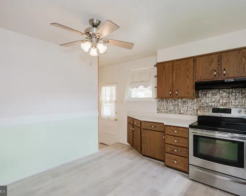 Kitchen with wooden cabinets, stainless steel oven, and a patterned tile backsplash; pale green lower wall and light wood floor.
