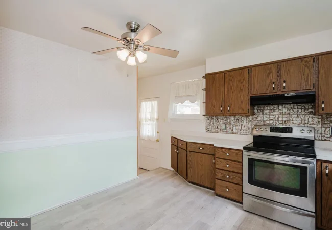 Kitchen with wooden cabinets, stainless steel oven, and a patterned tile backsplash; pale green lower wall and light wood floor.