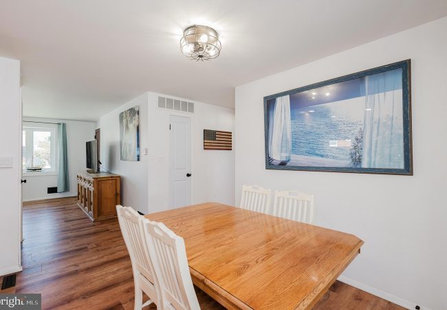 Dining room with a wooden table and white chairs; large ocean-view artwork on the wall and an American flag nearby.
