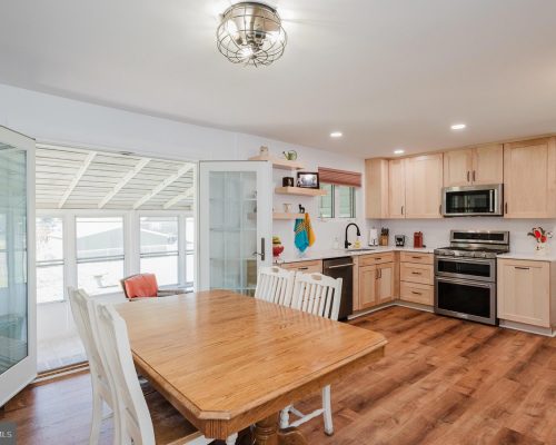 Bright kitchen with light wood cabinets, stainless steel stove/oven, and a wooden dining table with white chairs in an open-plan space