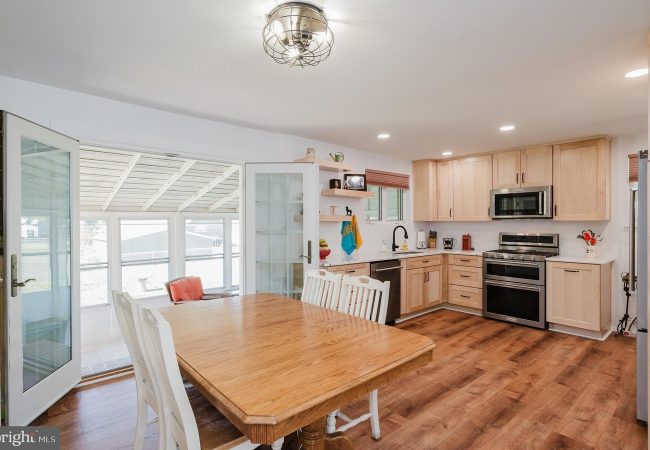 Bright kitchen with light wood cabinets, stainless steel stove/oven, and a wooden dining table with white chairs in an open-plan space