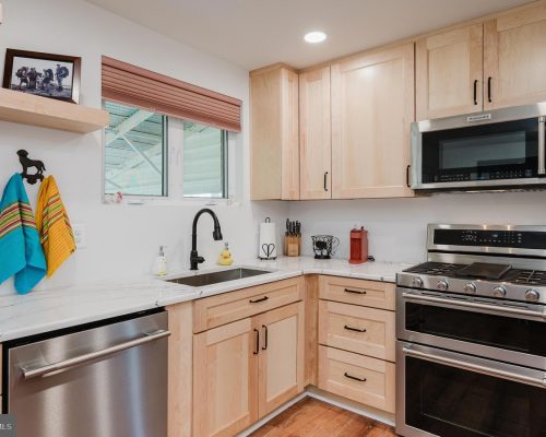 Modern kitchen with light wood cabinets, stainless steel double-oven range and microwave, white marble counters, and a window.