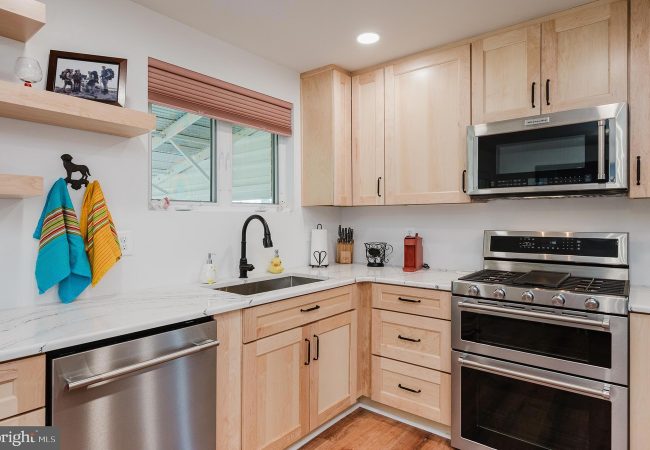 Modern kitchen with light wood cabinets, stainless steel double-oven range and microwave, white marble counters, and a window.