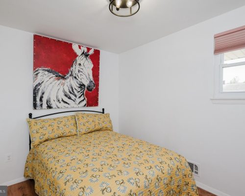 Small bedroom with a black metal bed, yellow floral duvet and pillows, and a red-and-white zebra painting above the headboard.