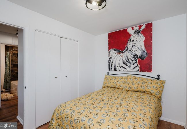 Small bedroom with white walls and a twin bed in a yellow floral quilt, black metal headboard, and a bold red zebra painting above the bed.