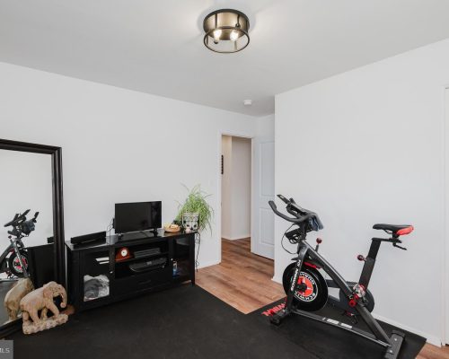 Home gym with a spinning bike on a black mat, a TV stand, and a tall mirror in a bright, minimalist room.