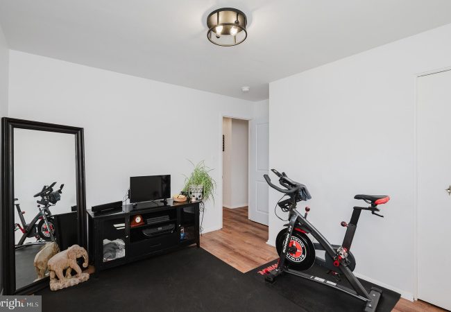 Home gym with a spinning bike on a black mat, a TV stand, and a tall mirror in a bright, minimalist room.