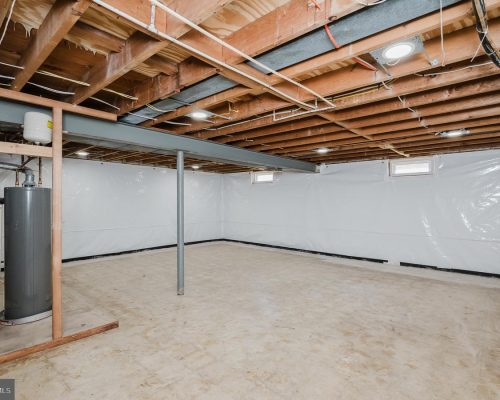 Unfinished basement with exposed joists, a grey water heater, a vertical support post, and white plastic-wrapped walls.