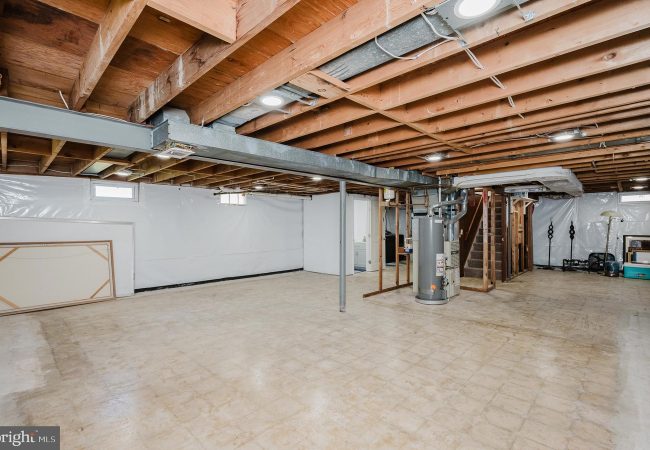 Unfinished basement with exposed wooden joists, a central furnace, and utility area along the back wall.