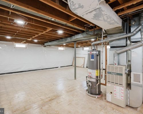 Unfinished basement utility area with exposed ceiling joists, ductwork, and a water heater next to a furnace.