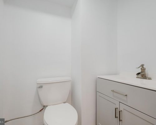 Small white bathroom with a toilet beside a light gray vanity and sink faucet.