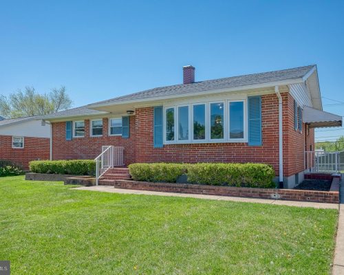 Front view of a brick ranch home with blue shutters, a large bay window, and neatly trimmed hedges along the front. The lawn is green and the walkway leads to brick steps.