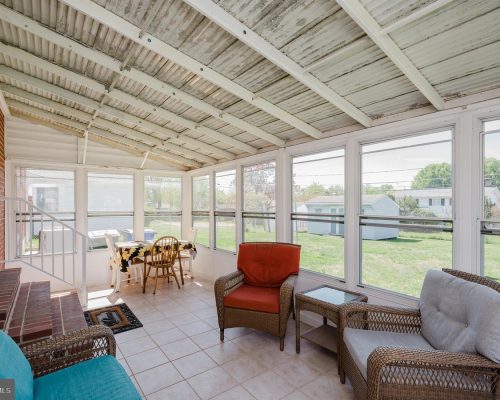 Bright sunroom with white-framed windows, wicker seating, and a small dining table overlooking a grassy backyard