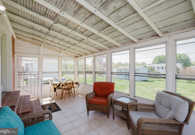 Bright sunroom with white-framed windows, wicker seating, and a small dining table overlooking a grassy backyard