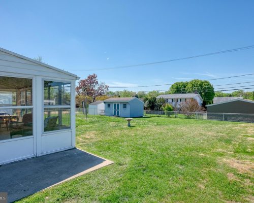Backyard with a white enclosed porch on the left, open green lawn, and a small blue shed under a clear blue sky.