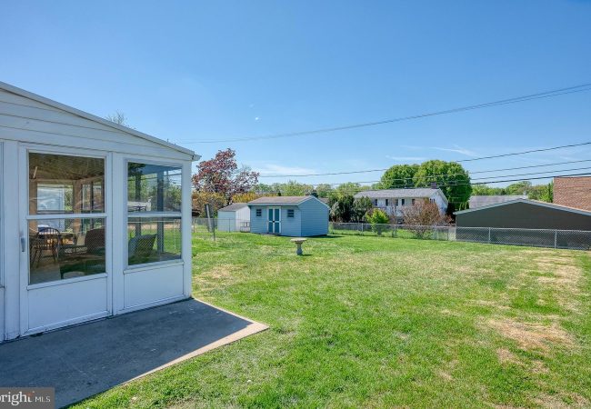 Backyard with a white enclosed porch on the left, open green lawn, and a small blue shed under a clear blue sky.