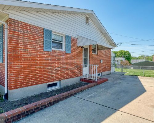 Brick ranch-style house with blue shutters, white awning over the entry, small front steps, and a concrete driveway.