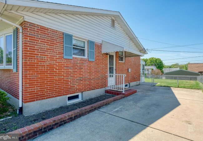 Brick ranch-style house with blue shutters, white awning over the entry, small front steps, and a concrete driveway.