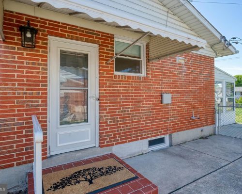 Brick house entry with a white door, small side window, and a tree-pattern doormat on a brick stoop under a white awning.
