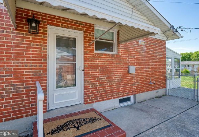 Brick house entry with a white door, small side window, and a tree-pattern doormat on a brick stoop under a white awning.