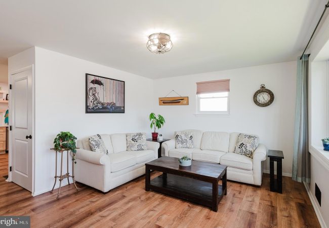 L-shaped white sofa set with patterned cushions, a dark wood coffee table, and potted plants in a bright living room.