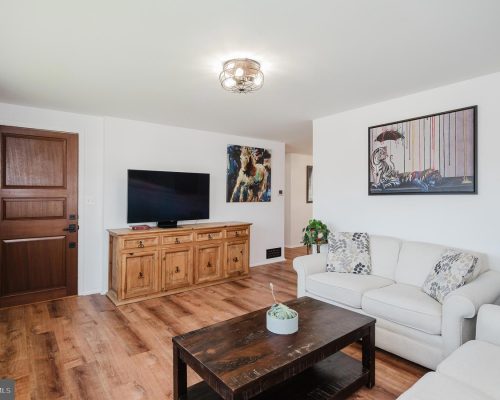 Living room with a flat-screen TV on a wooden cabinet, beige sofa, and a dark coffee table.
