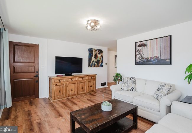 Living room with a flat-screen TV on a wooden cabinet, beige sofa, and a dark coffee table.