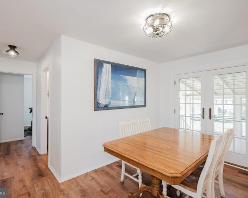 Bright dining room with a wooden table and white chairs, glass French doors, and a sea-themed wall art above the wall outlet edge.