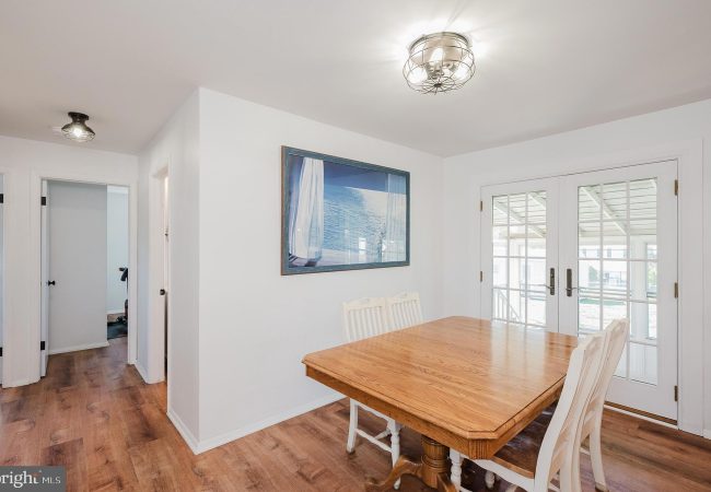 Bright dining room with a wooden table and white chairs, glass French doors, and a sea-themed wall art above the wall outlet edge.