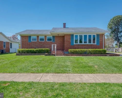 Brick ranch-style house with a gray roof, blue shutters, and a well-kept green lawn.