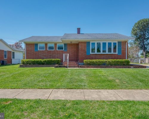Front view of a single-story brick house with blue shutters, a small set of steps, and neatly trimmed hedges in front yard.